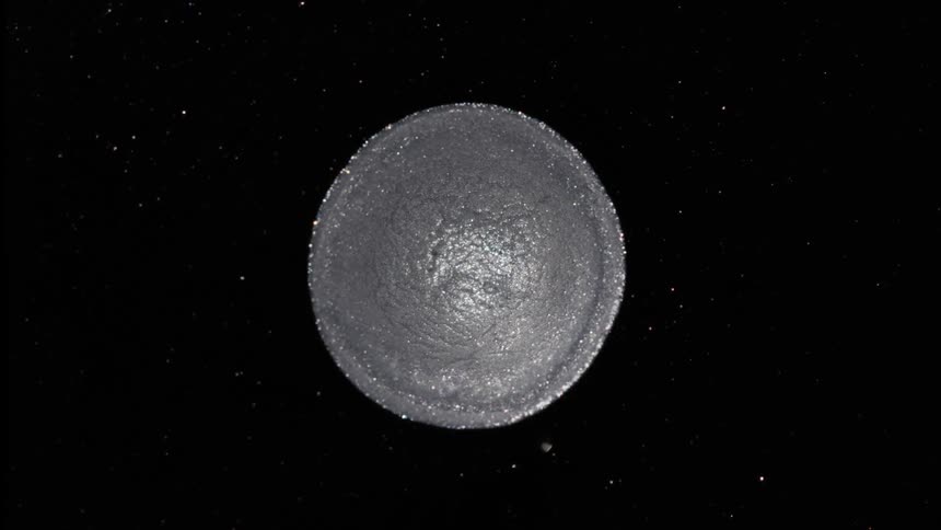 A small circle of silver powdery material has circular ripples that spread across its surface