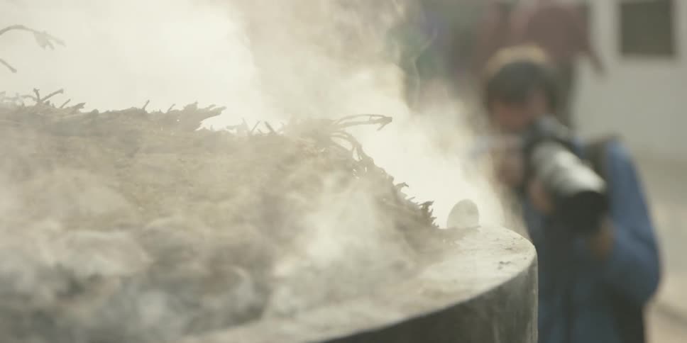 Smoke rises from a large urn as a photographer takes pictures of something near it