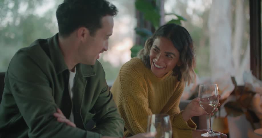 A man with a smart phone sitting on a couch with a woman in front of a table with a laptop
