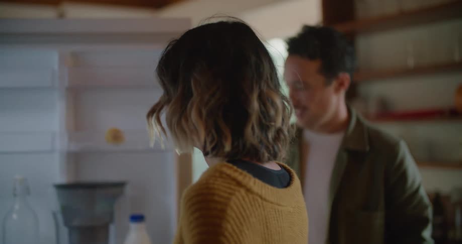 A couple carry groceries into their kitchen and open the fridge