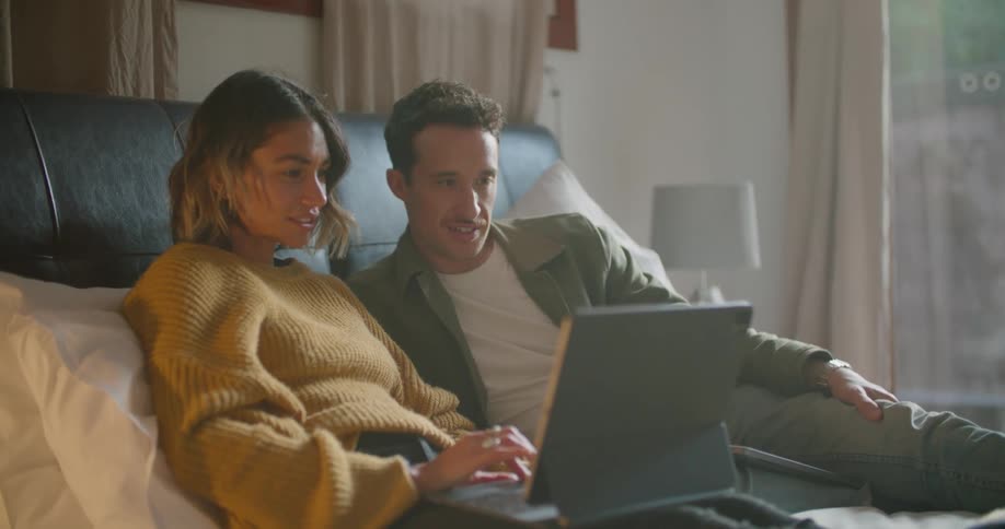 A man and woman laying in bed looking at a laptop