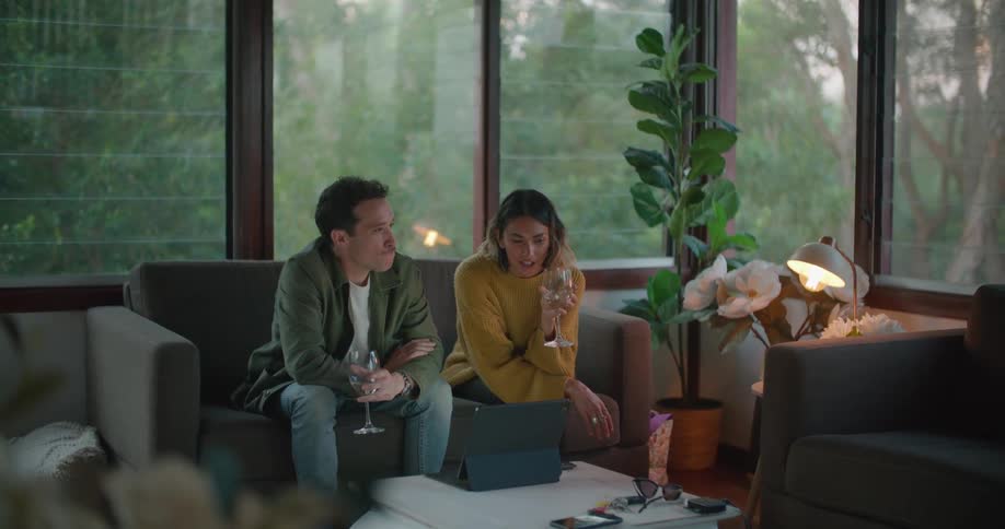 A man and woman sitting on a couch drinking wine