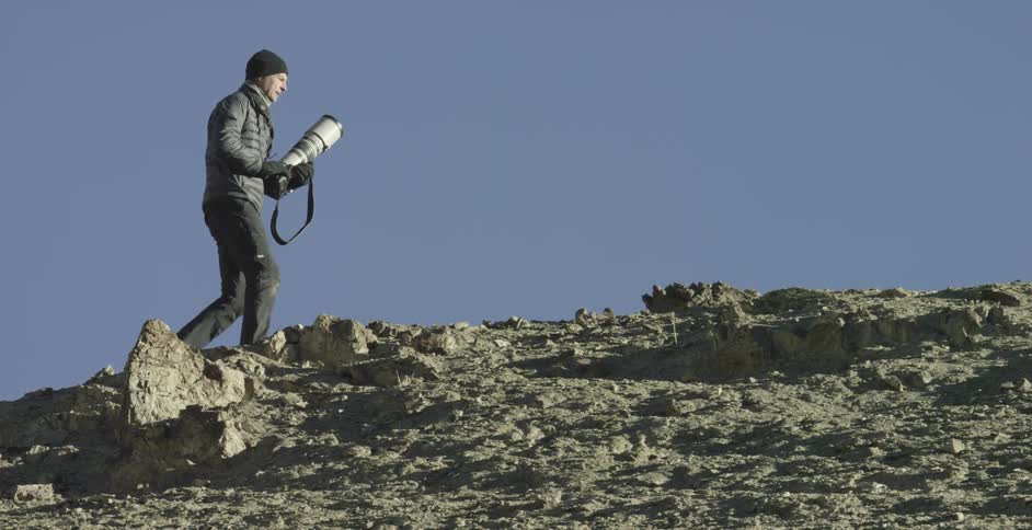A person carries a camera up a rocky hill