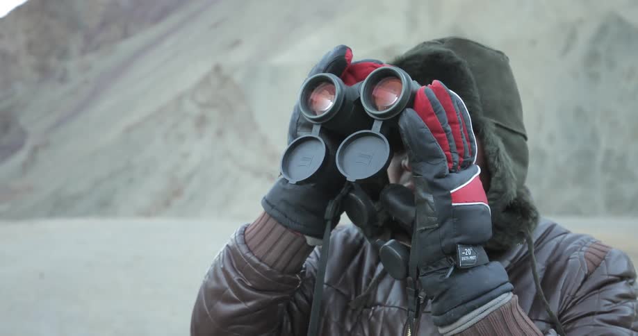 A man in winter gear looks through binoculars
