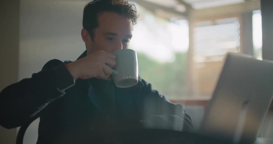 A man grabbing a drink while using a laptop