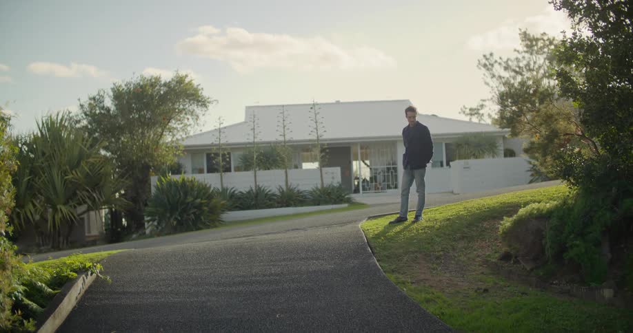 A man stands on the grass next to a driveway as his stares downhill