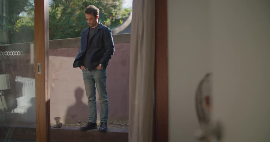 Man with dark jacket and jeans checks his smartphone and enters room