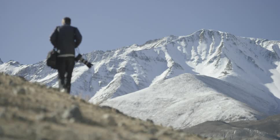 A man holding a large camera walks uphill