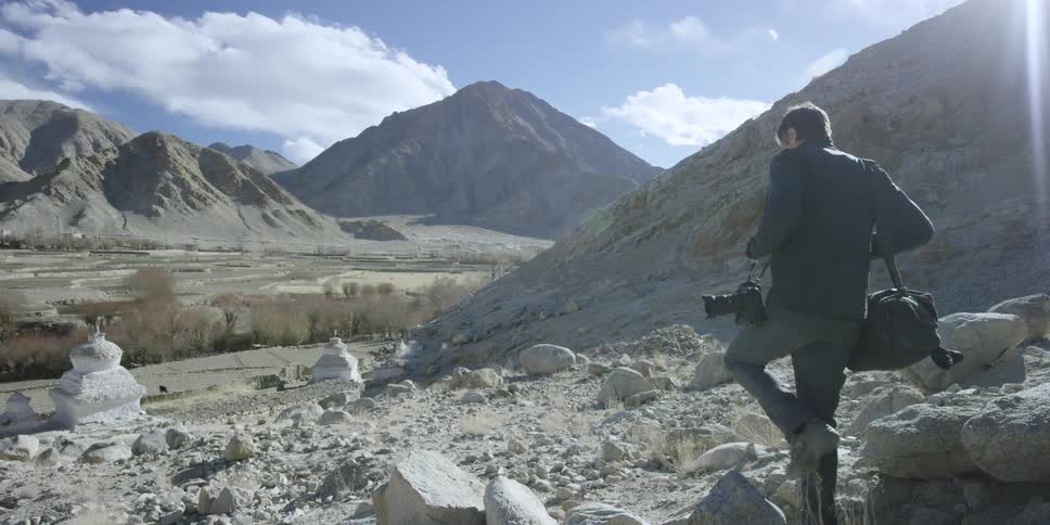 A man carries a camera over a rocky area