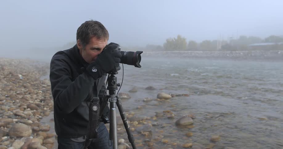 A photographer with his camera on a tripod, takes pictures near a mist covered river