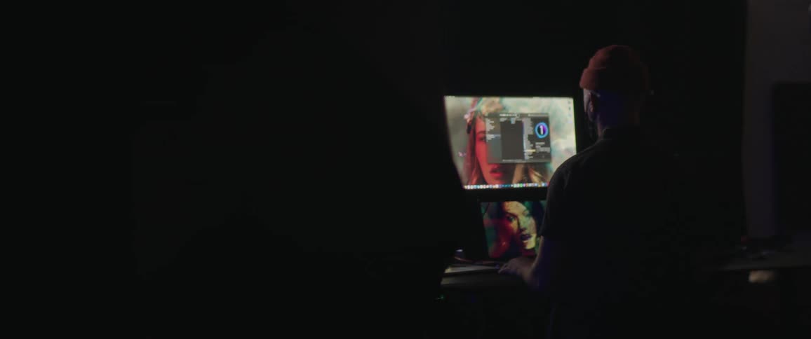 The silhouette of a man can be seen as he sits in front of a computer while manipulating digital imagery