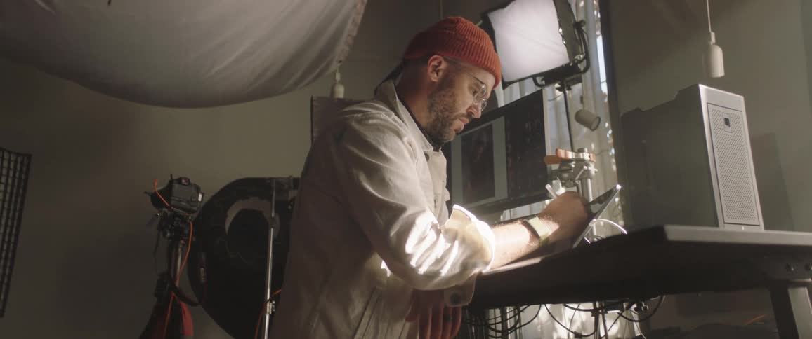 A man with a hat in a studio using a tablet with a stylus