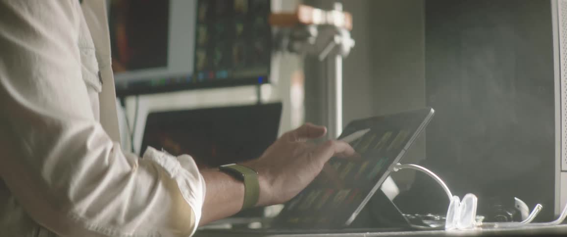 A man is sitting at a desk and scrolling on an electronic tablet