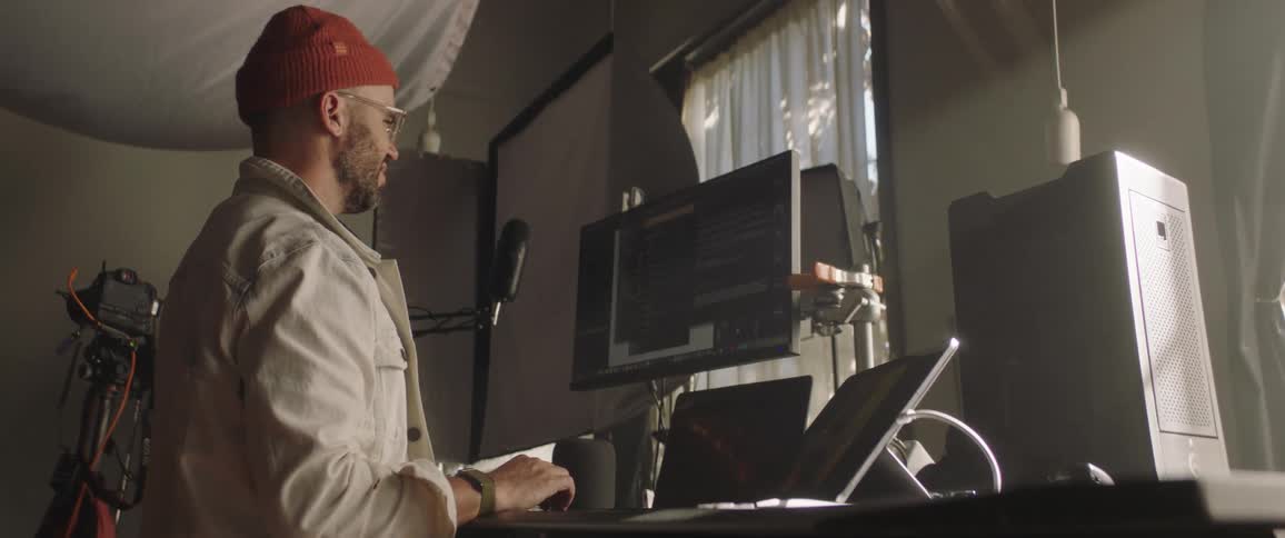 A man stands in front of a computer work station while scrolling on one of the screens indoors during the day