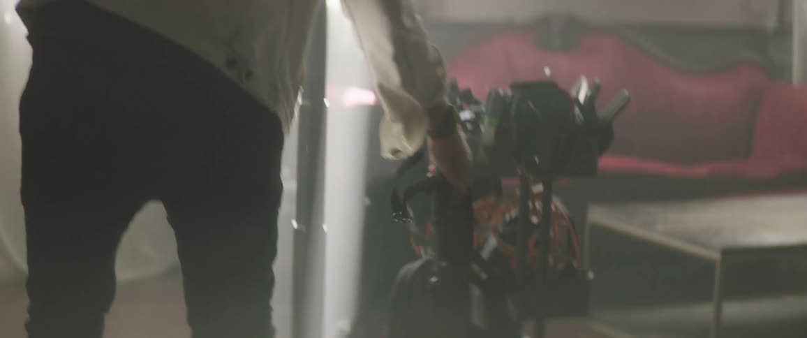 Man wearing jacket sets backpack on wooden floor in room with large screen