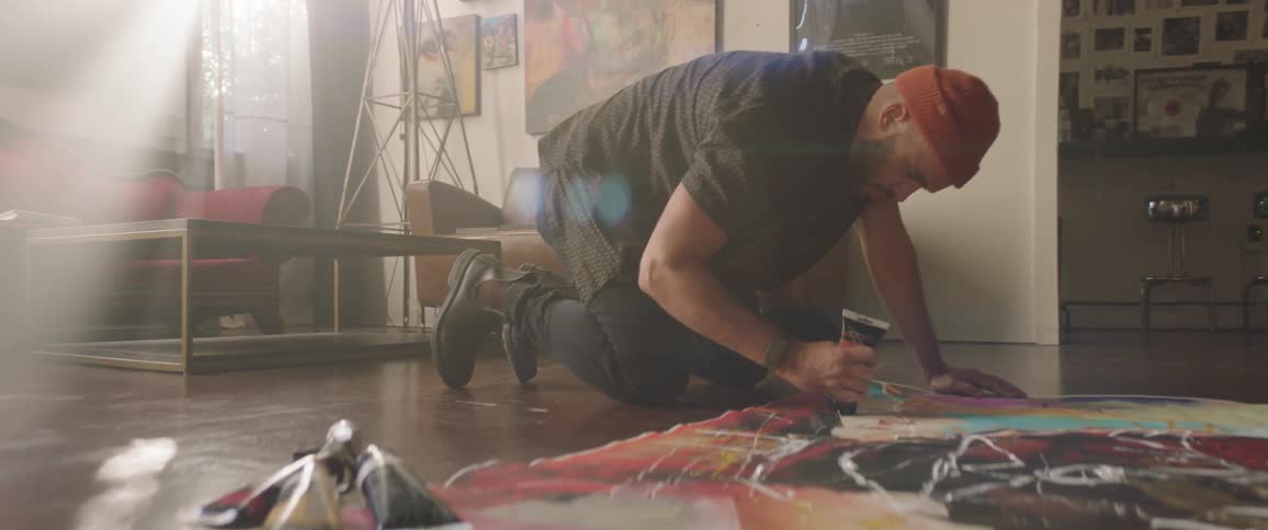 A man squeezes a tube of paint on a large canvas on the floor