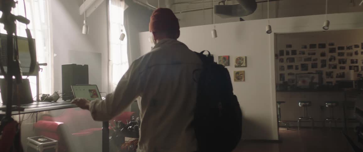A man with a hat and backpack walking up to a desk and using a computer