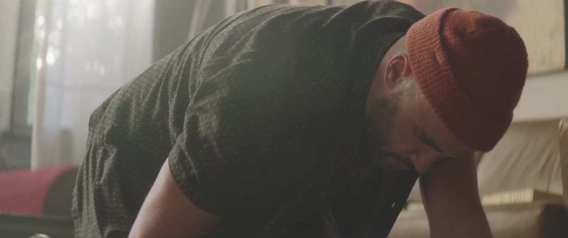 Man applies paint from a tube onto a canvas while he kneels on the floor