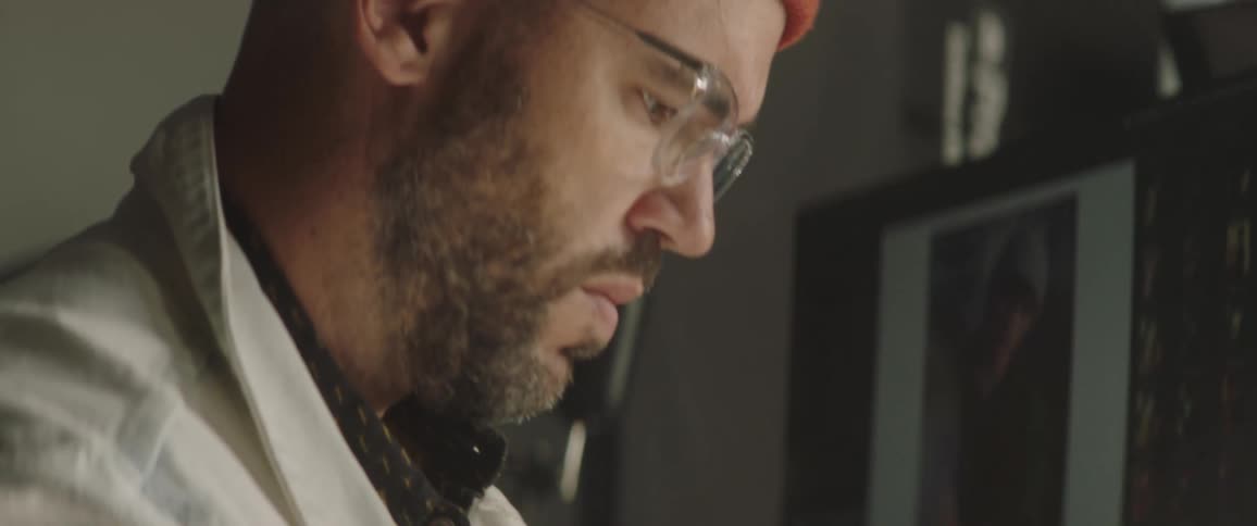 A man wearing glasses and a beanie concentrates as he uses his computer