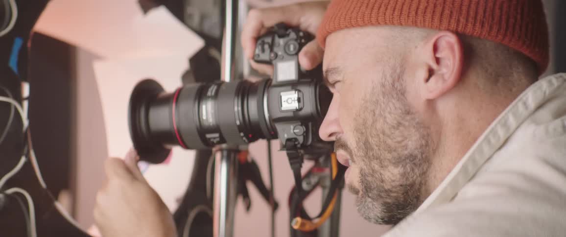 A man with a hat taking pictures with a camera in the studio with a wall in the background