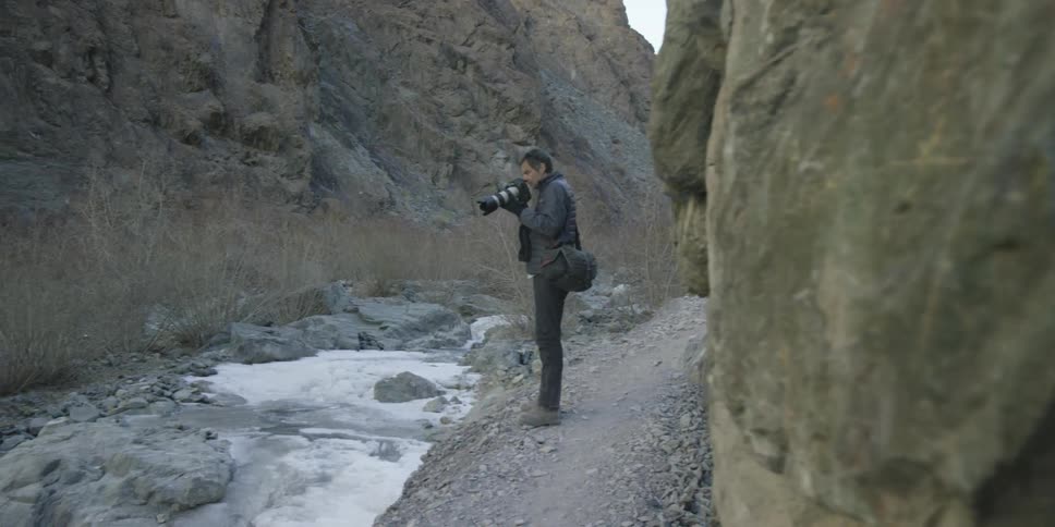 A man is standing over an ice covered stream taking photographs