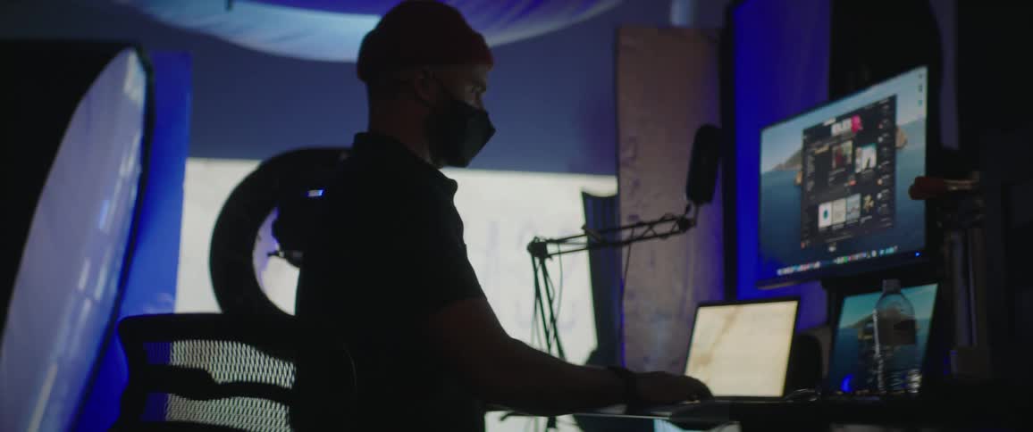 A man in a room with a hat and mask using a computer