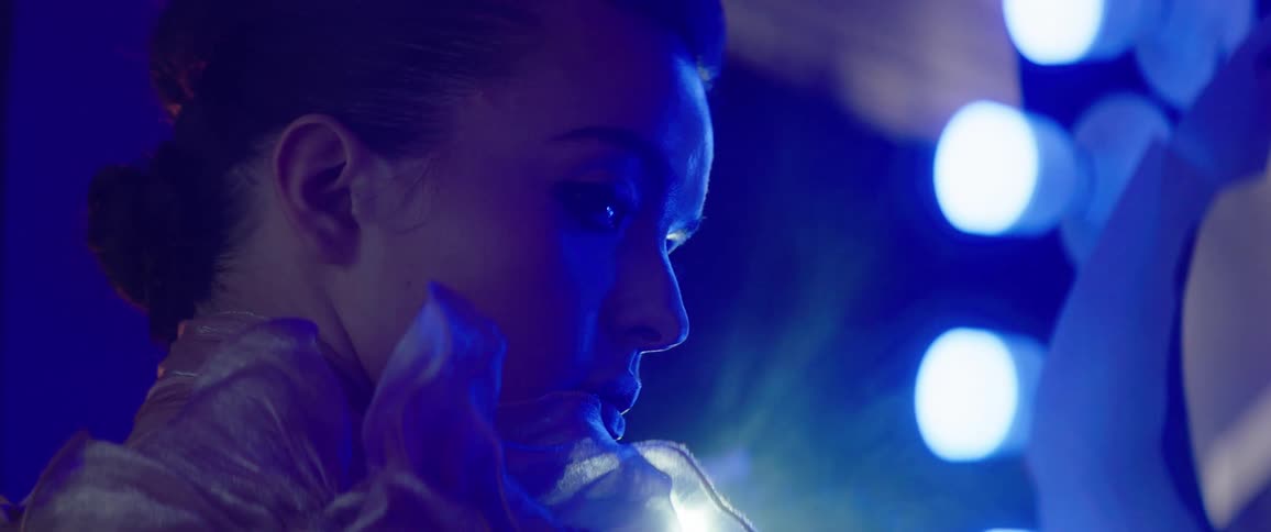 A woman posing at a photo shoot indoors in front of a lighting device with a flare from a light beaming behind her