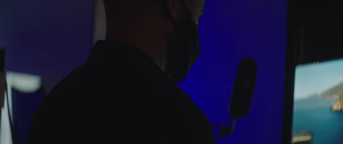 Man with a black mask works on a desktop and a laptop in the studio