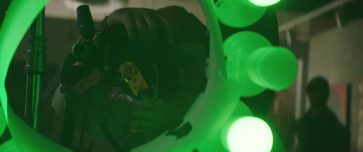 Male photographer takes pictures through ring made of colorful lights as another person waits in background