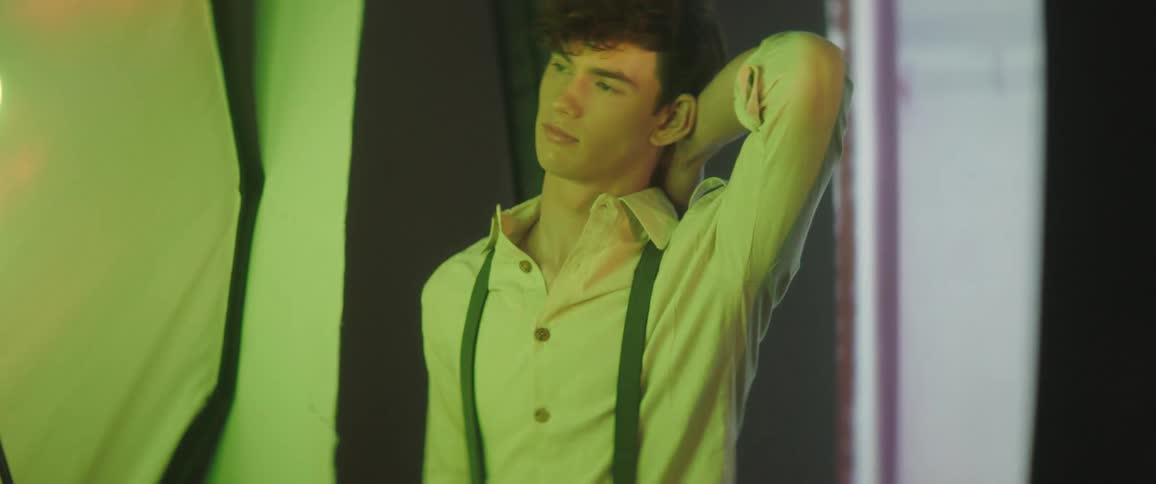 A male model poses in a button down shirt and suspenders with his arm behind his head