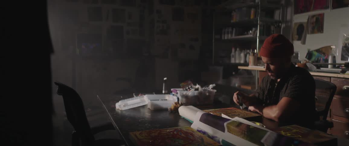 Artist painting with oil over a desk inside a dimly lit studio