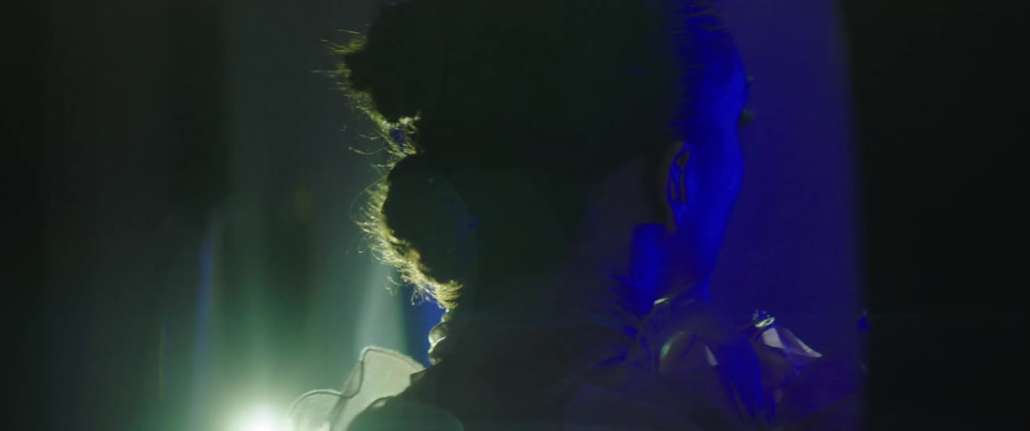 A young woman poses for photographs while in a dark room and illuminated with blue light