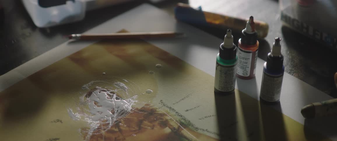 Three bottles of paint on top of a table next to a piece of artwork indoors