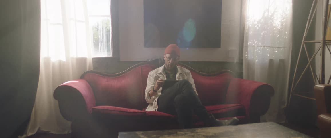 A man with a hat sitting on a couch using a tablet with a stylus
