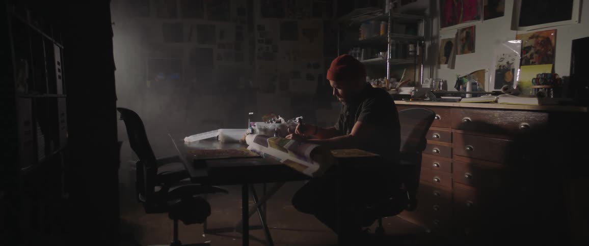 A man with a hat in a room sitting on a chair at a table