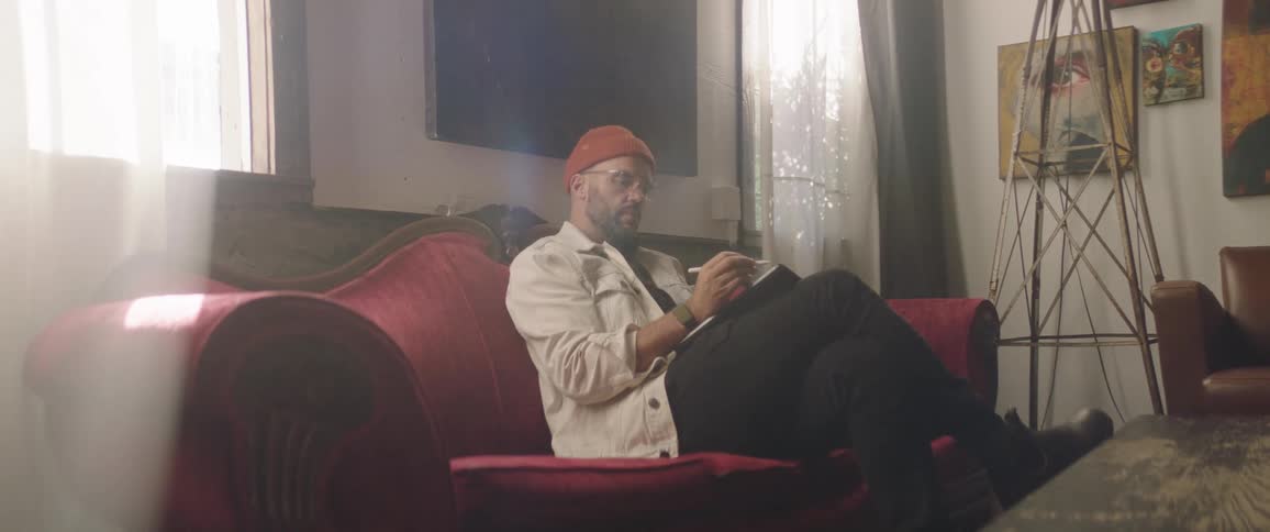 Man sits on sofabetween windows drawing on tablet