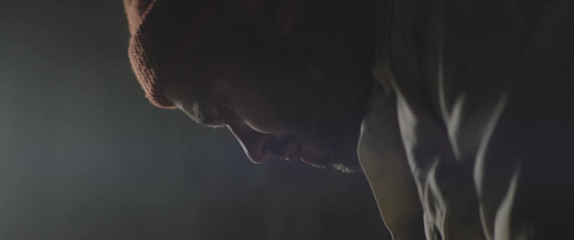 Man wearing a beanie concentrated over his work inside a dimly lit studio