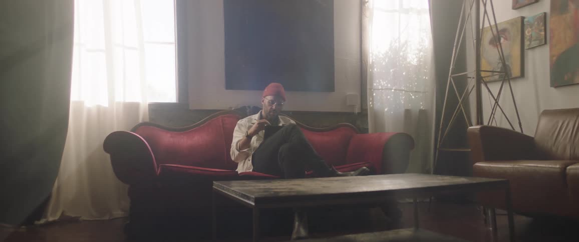 A man with a hat sitting on a couch using a tablet with a stylus