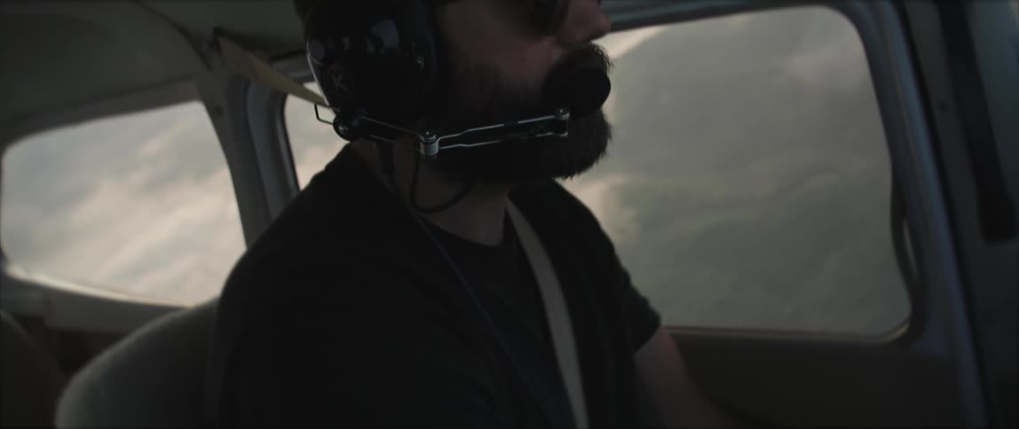 A man with a headset and sunglasses flying an aircraft with the sky and clouds in the background