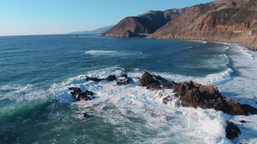 Ocean waves roll into mountainous shore