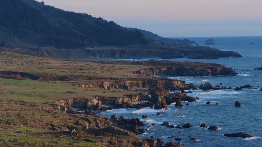 The green shore line is surrounded by crashing waves