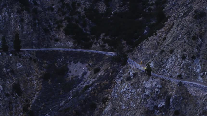 A vehicle is driving on a winding road in a natural landscape at dusk