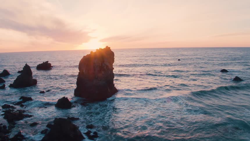 Ocean waves roll into shore near the mountains as the sun rises