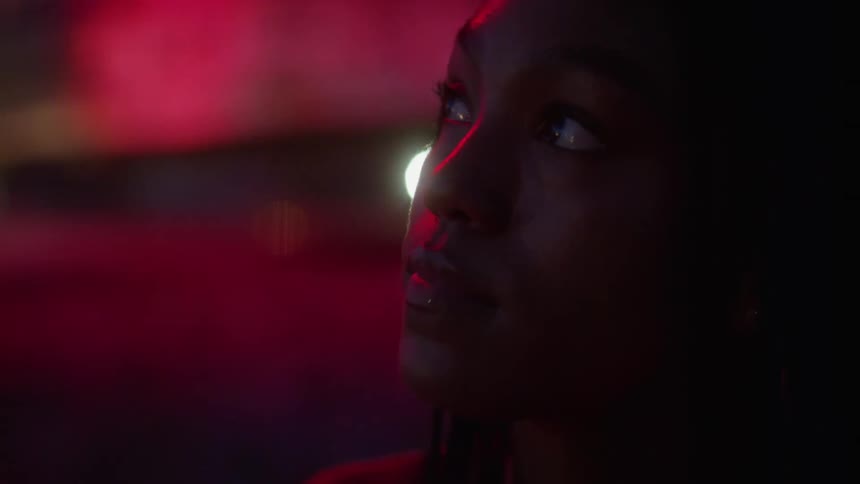 Woman looks around at night as traffic passes by in background
