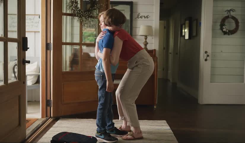 Angry young boy throws his school bag on the floor and his mother rushes to him to hug and comfort him