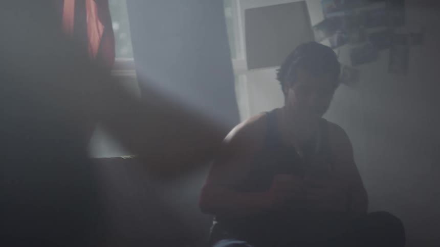 A man sitting on a long couch takes his smartphone out of his back pocket to record a woman dancing