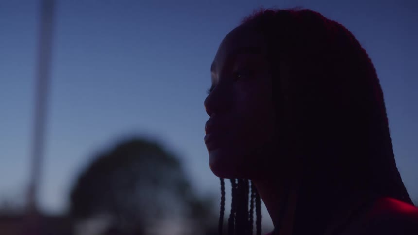 A woman with long braids sits outside alone at night