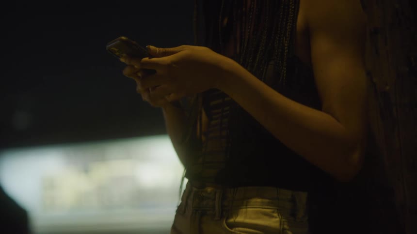 Woman leans against streetlight pole near street checking her mobile phone
