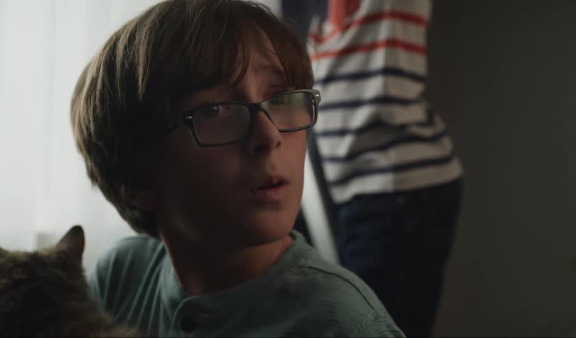 A boy holding a cat turns around in surprise to look at something out of frame