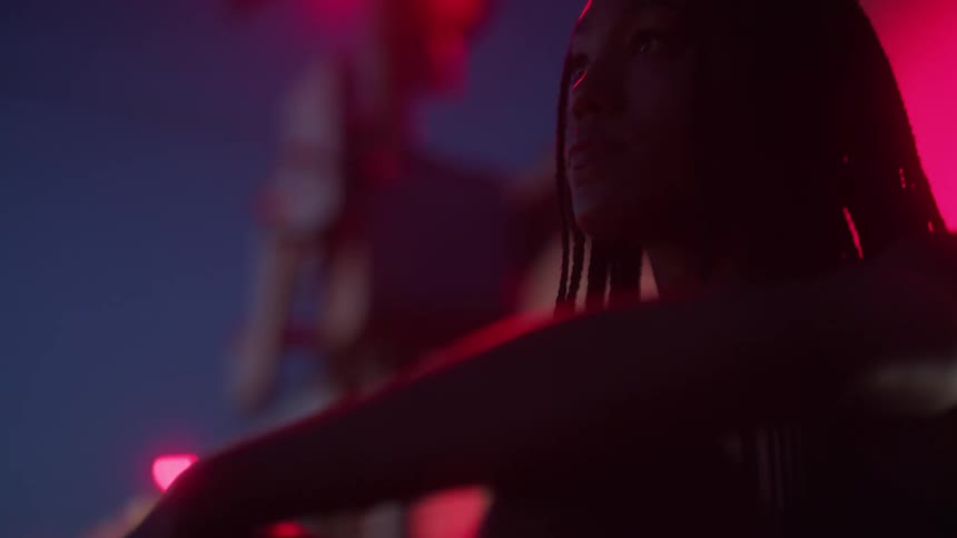 A young woman sits with her back to a train track as a train passes by at night